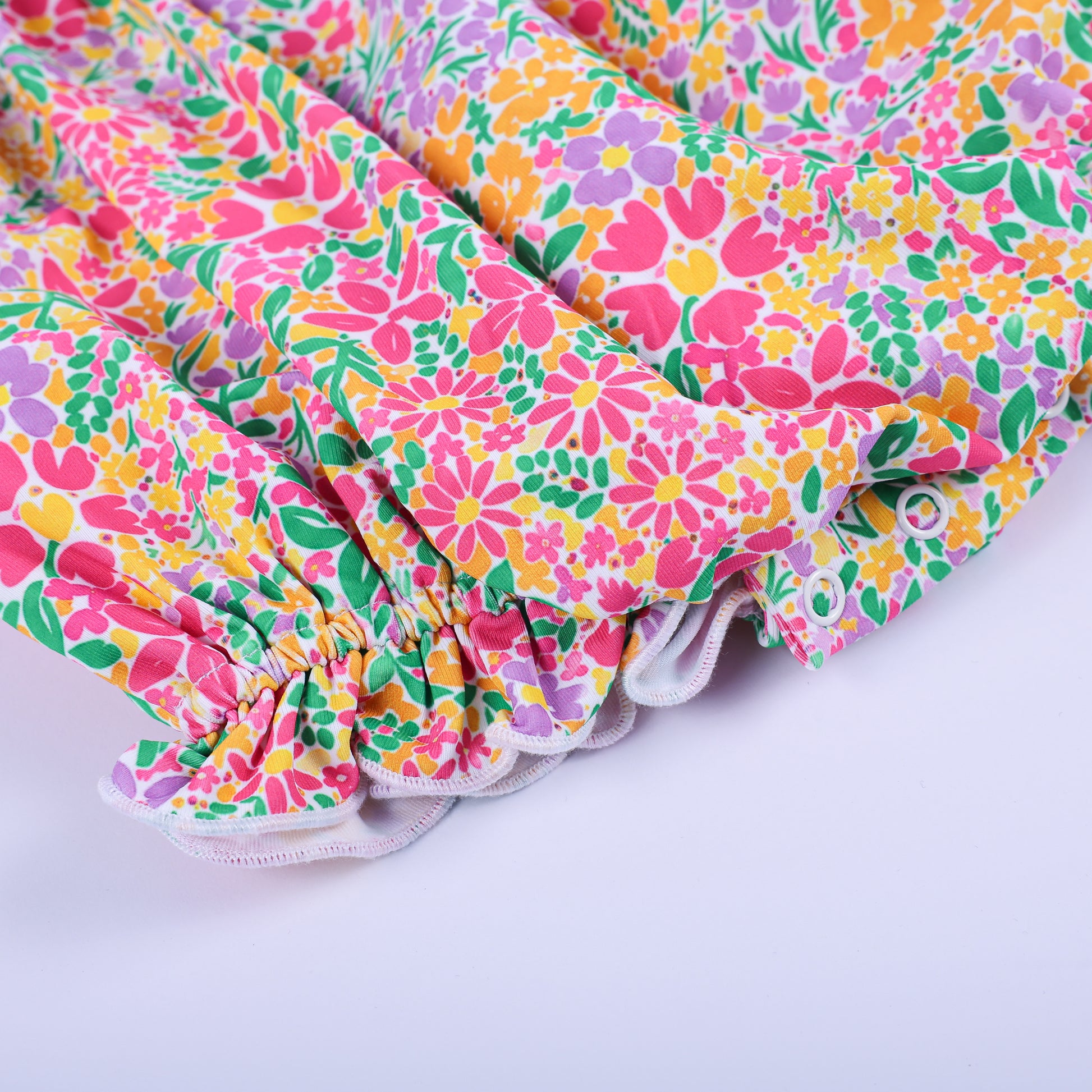 Close-up of the ruffled leg opening and snap button closures on the pink floral Thanksgiving baby bubble romper.