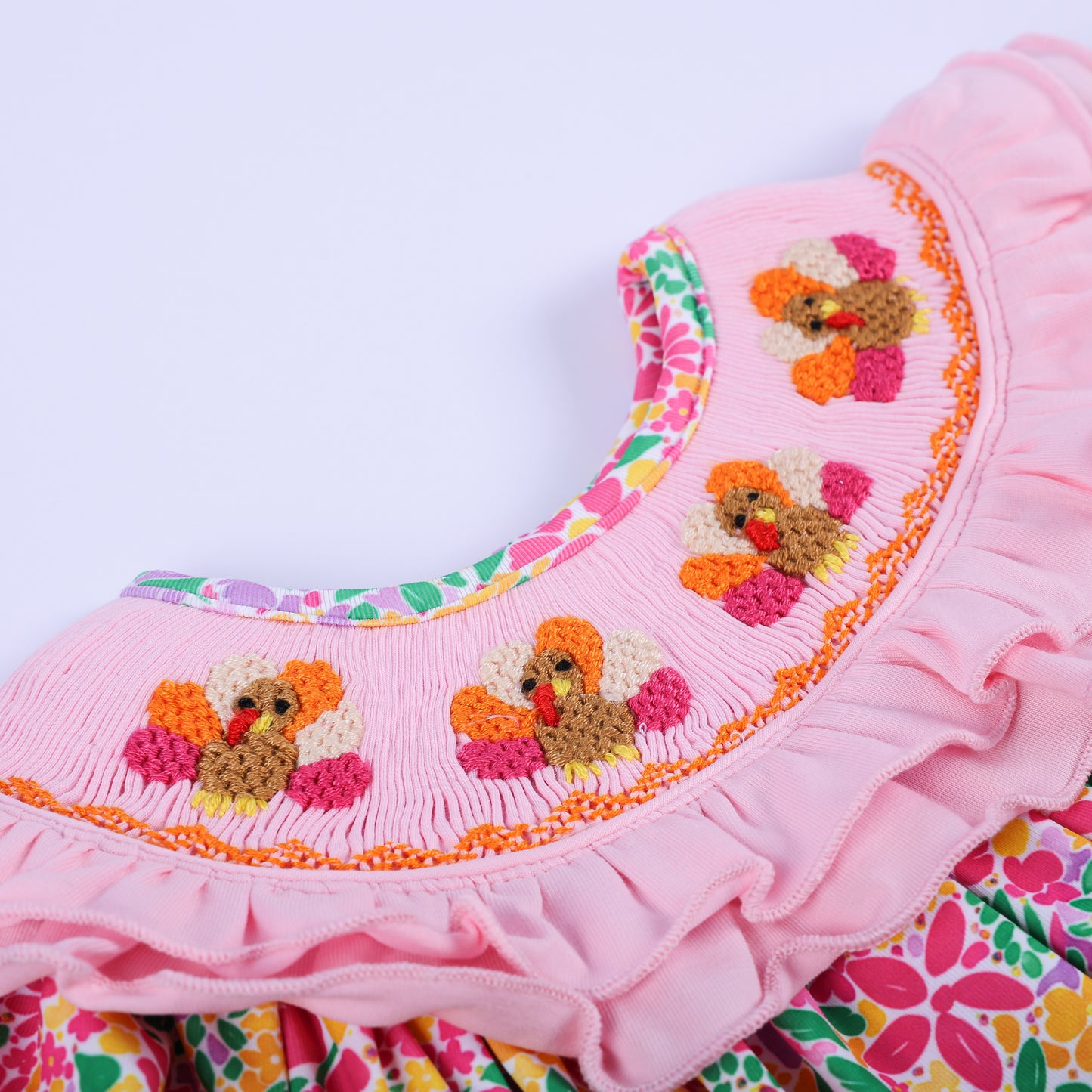 Close-up detail of the pink smocked ruffled collar with hand-embroidered Thanksgiving turkeys on a baby bubble romper.
