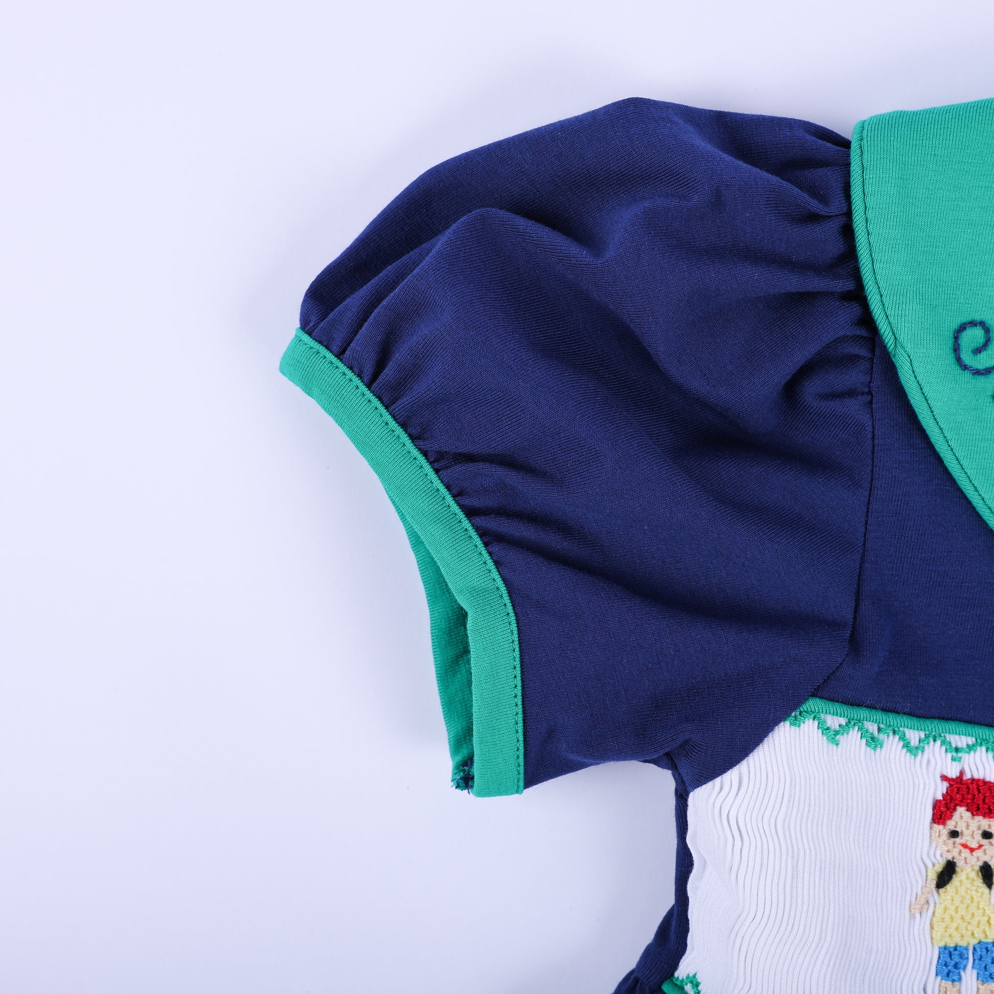 Sleeve detail of the navy 'Jesus Loves the Little Children' smocked dress, showing the puffed design and green trim.