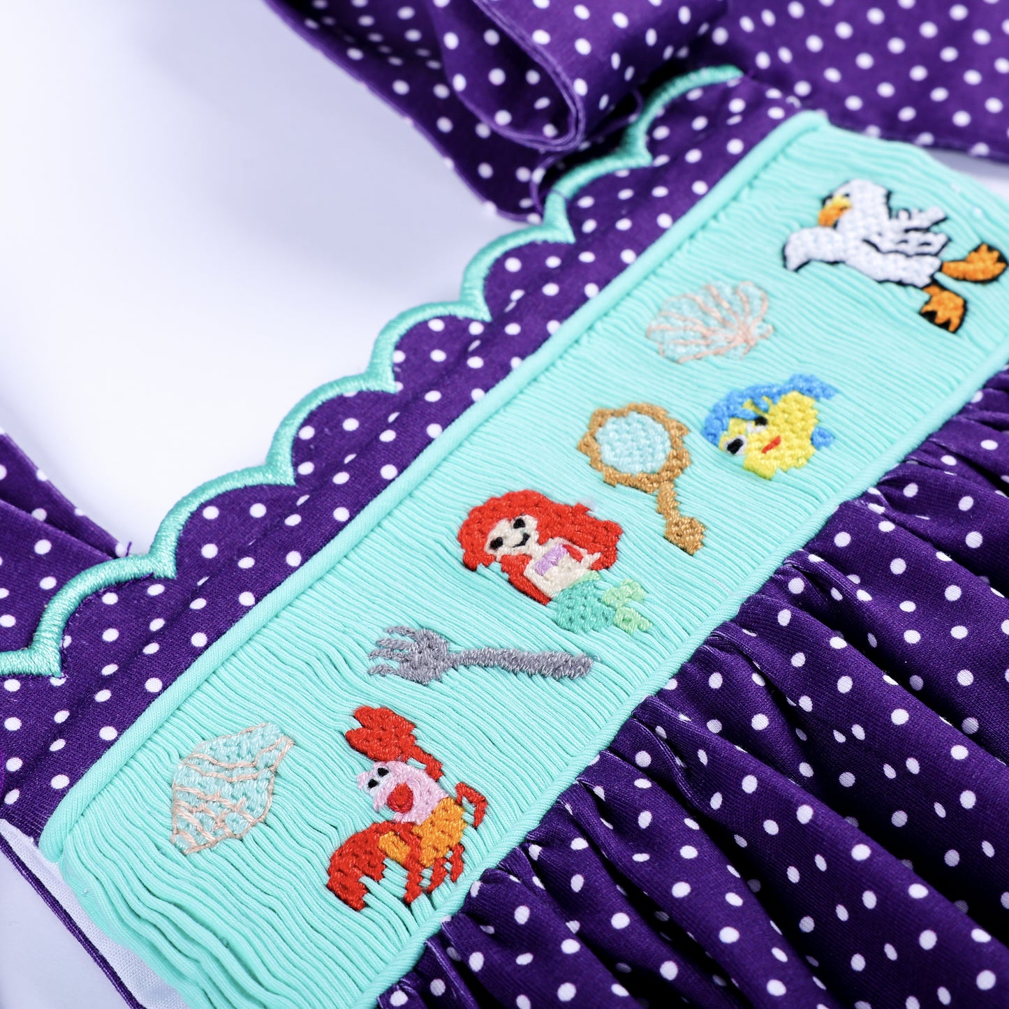 Close-up of hand smocked ocean plate featuring mermaid, crab, fish, and seagull hand embroidery details.
