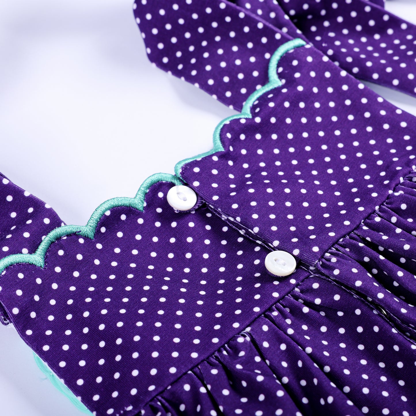 Close-up view of white back buttons and scalloped mint trim on purple polka dot hand smocked bloomer set.