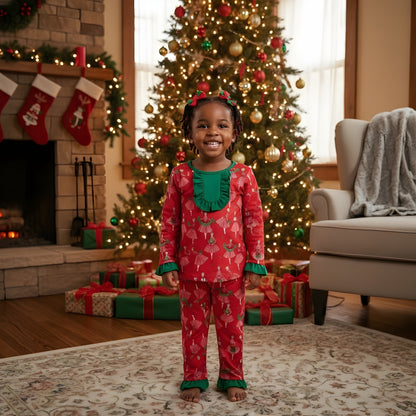 Toddler girl wearing Vintage Christmas Lady Icons red pajama set with green ruffle trim standing by tree.