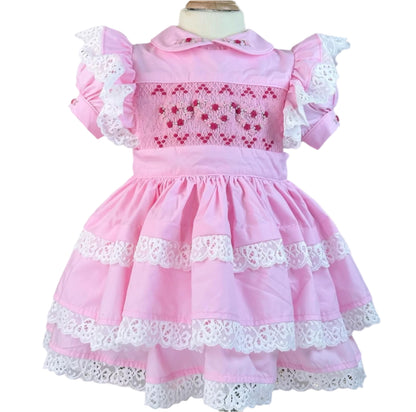 Pastel pink vintage Valentine heirloom dress featuring hand-smocked red hearts, embroidered rosebuds, and lace-trimmed tiers by Smocked Peacock.